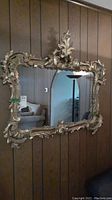 Mirror hung on wooden paneled wall showing full ornate frame and reflective surface.