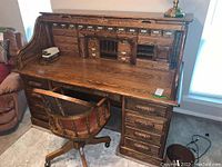 Front view of oak roll-top desk with matching rolling chair and visible carvings