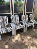 Four aluminum framed patio chairs with striped cushions, arranged in a row outside on concrete patio, showing the overall condition and wear.