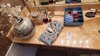 Countertop with assorted vanity items including hair combs, lidded containers, drawstring pouch, and ceramic decorative vessel.