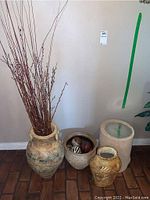 Four different decorative flower pot planters shown together to demonstrate variety and size differences, positioned on a brick floor against a wall.