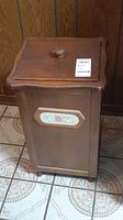 Full view of wooden potato bin with hinged lid and knob handle sitting on tiled floor.