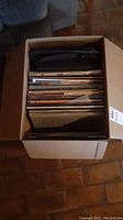 Box with multiple vinyl record albums stored upright inside a cardboard box.