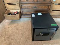 Black and gray SentrySafe security safe on carpet near wooden dresser drawers