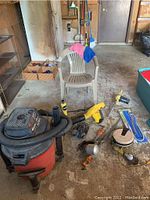 Craftsman shop vacuum, yellow blower, electric chainsaw, plastic chair, and assorted tools on garage floor