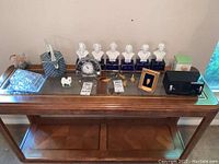 Lot shown on glass and wood table featuring six bust statues, glass dish, dog figurine, radio, clock, tin, and small framed items