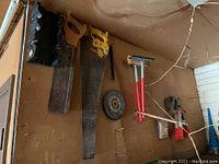 Hand saws hanging on the wall with other tools including a squeegee, clamp, and circular saw blade.