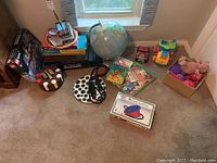 Lot on floor showing a collection of board games, LEGO set, poker chips, traveling globe, toys and books near window.