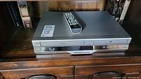 Full view of silver Toshiba DVD and VCR combo player with remote on top, sitting on a wooden shelf with books.