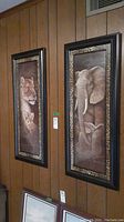 Two framed animal portraits on wood-paneled wall; lioness and cub on left, elephant and calf on right with black and leopard print frames.