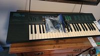 Full view of Yamaha PSR-6 keyboard with keys, control panel, and cables placed on top in plastic bag, showing overall condition and included accessories.