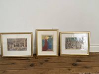 Full view of three gold framed prints arranged side by side on floor, showing proportions and frame style.