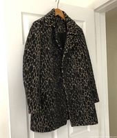 Leopard print double breasted coat hanging on white door, showing full front and sleeves