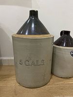 Full view of the larger 5 gallon jug marked 5 GALS with a beige body and dark brown neck.