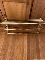 Full view of brass towel rack shelf on wood floor leaning against cabinet.
