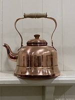Front view of the copper teapot showing its body, spout, wooden handle and lid knob.