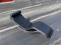 Full side perspective of leather chaise pad, headrest pillow, and chrome frame segments on asphalt