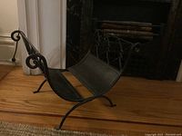 Side angle view of the folding wrought iron log holder, showing curved base and scroll detailing