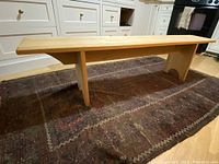Full side angle photo of a handmade wooden bench in a kitchen setting, showing length and legs structure.