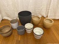Group photo showing eight planters of varying sizes and materials on a wooden floor against a white backdrop, illustrating the size and condition of each planter.