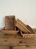 Four large tray-shaped wicker baskets arranged on wooden floor showing shape and size