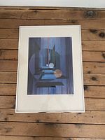 Framed colored lithograph print with abstract geometric shapes in blue and purple tones, displayed on a wooden surface.