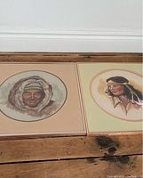 Overall view of both framed pastel portraits laid flat on a wooden floor