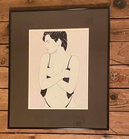 Full view of the framed Patrick Nagel print showing the woman's upper body in black bikini with arms crossed, mounted on a wooden background.