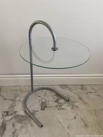 Side view of the vintage Ikea Ry side table showing the glass tabletop held by a curved aluminium frame base.