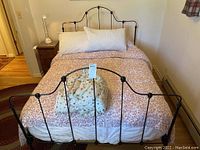 Full view of assembled full size black iron bed frame with floral linens and white pillows