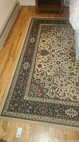Full view of the polyester area rug showing the floral pattern and border design on hardwood floor, lot contents.