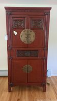 Front view of Asian-style cabinet showing carved doors, brass hardware, and drawer
