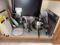 Cutting boards, marble cheese board, Revere Ware pots, fry pans, and baking trays arranged in kitchen cabinet.