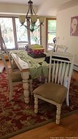 Set of six white wooden dining chairs arranged around a dining table with tablecloth and items on it.