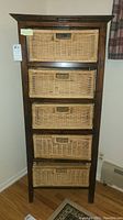 Front view of tall wooden dresser with five woven wicker baskets as drawers.