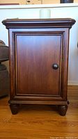 Front view of the solid wood end table showing paneled door and round black knob with flameless candle on top.