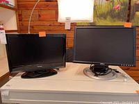 Two flat screen monitors side by side on a white table, Toshiba on the left and Dell on the right, both powered off.