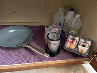 Magic Bullet blender, GreenPan skillet, and boxed Bodum glasses shown inside cabinet