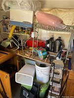 Large lot showing a bench with tools, plant stands, plastic containers, buckets, and small power tools below.