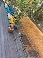 Faux tree in brown ceramic planter on rolling platform beside metal bench, several planters lined up