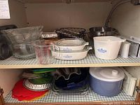 Under cabinet shelf showing assortment of glass Pyrex bowls, CorningWare casseroles and other baking dishes, muffin tins, pie tins and metal wire basket