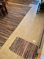 Photo of the large 6x9 ft rag rug displayed on tile floor alongside one of the smaller rugs.