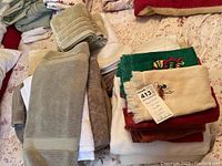 Pile of assorted bath towels, kitchen towels, and washcloths on floral bedding.