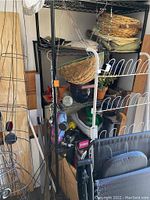 Wide view of black metal wire shelving rack with baskets, pots, Toro blower box, and gardening items including tomato cages and wooden planks behind it.