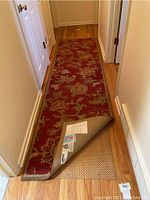 Runner rug laid out in a hallway, showing length and design with corner flipped to reveal pad underneath.