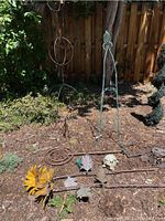 Photo of assorted metal and ceramic yard art displayed outdoors on soil, including geometric and floral metal stakes and ceramic decorative pieces.