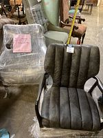 Front angle view of one grey leather chair showing channel-tufted seat and back, dark wood frame