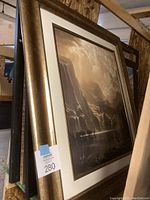 Framed landscape art with waterfall in gold-tone frame on storage shelf.