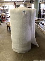 Full view of large white filler roll standing upright in warehouse environment.