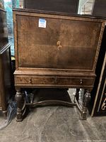 Full view of the wooden cabinet showing the front panel with floral inlay, drawer, and ornate legs.